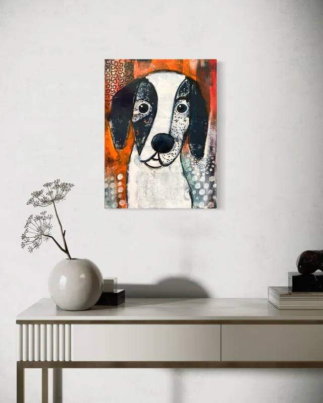 Ein moderner Konsolentisch mit einer weißen Vase mit Zweigen und einem schwarzen Dekorationsobjekt steht vor einer weißen Wand. Darüber hängt ein buntes abstraktes Gemälde eines Hundes mit weißem Gesicht und großen schwarzen Ohren.
